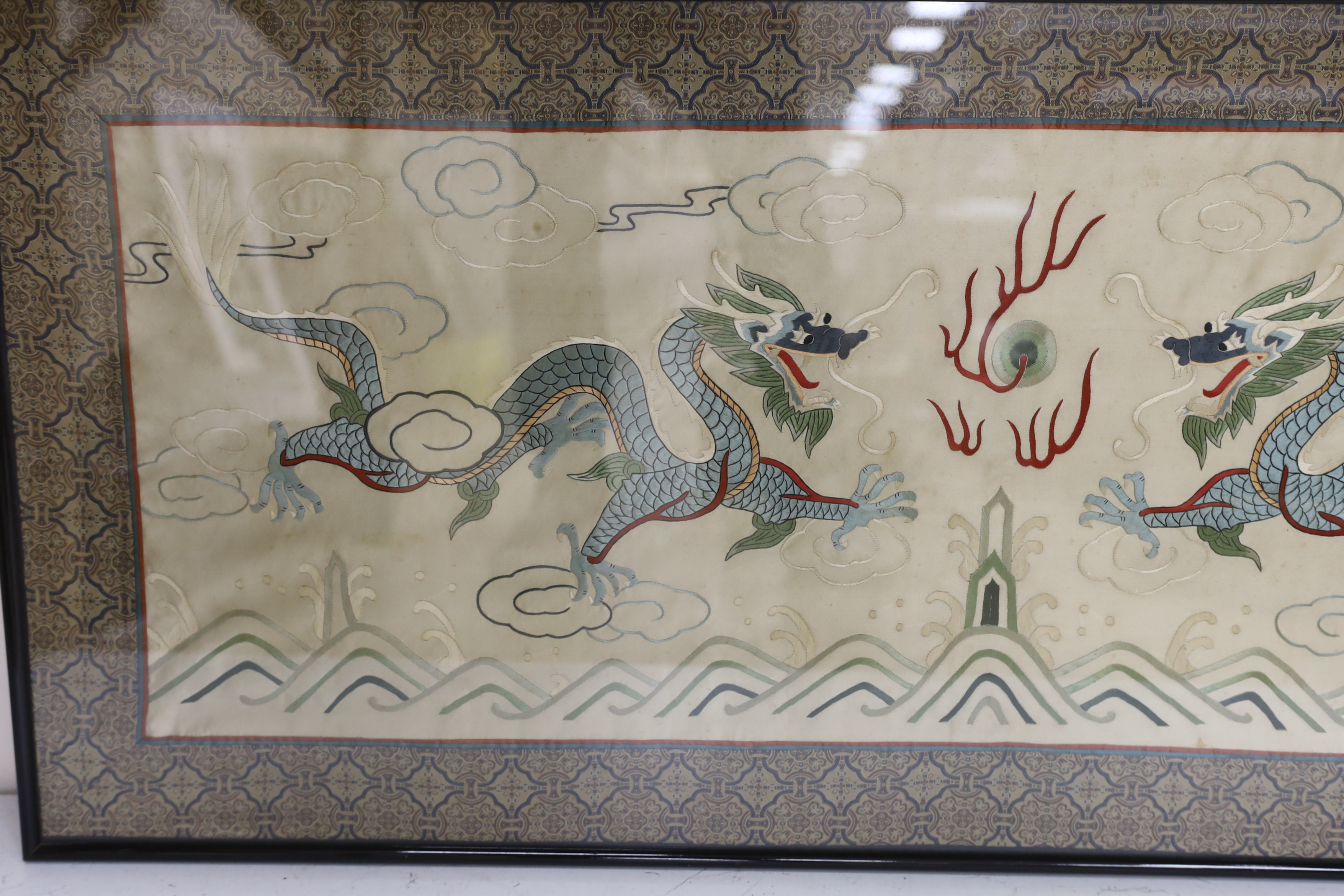 A framed 20th century Chinese silk embroidered 'dragon’ panel, with flaming pearl design, bordered with silk brocade